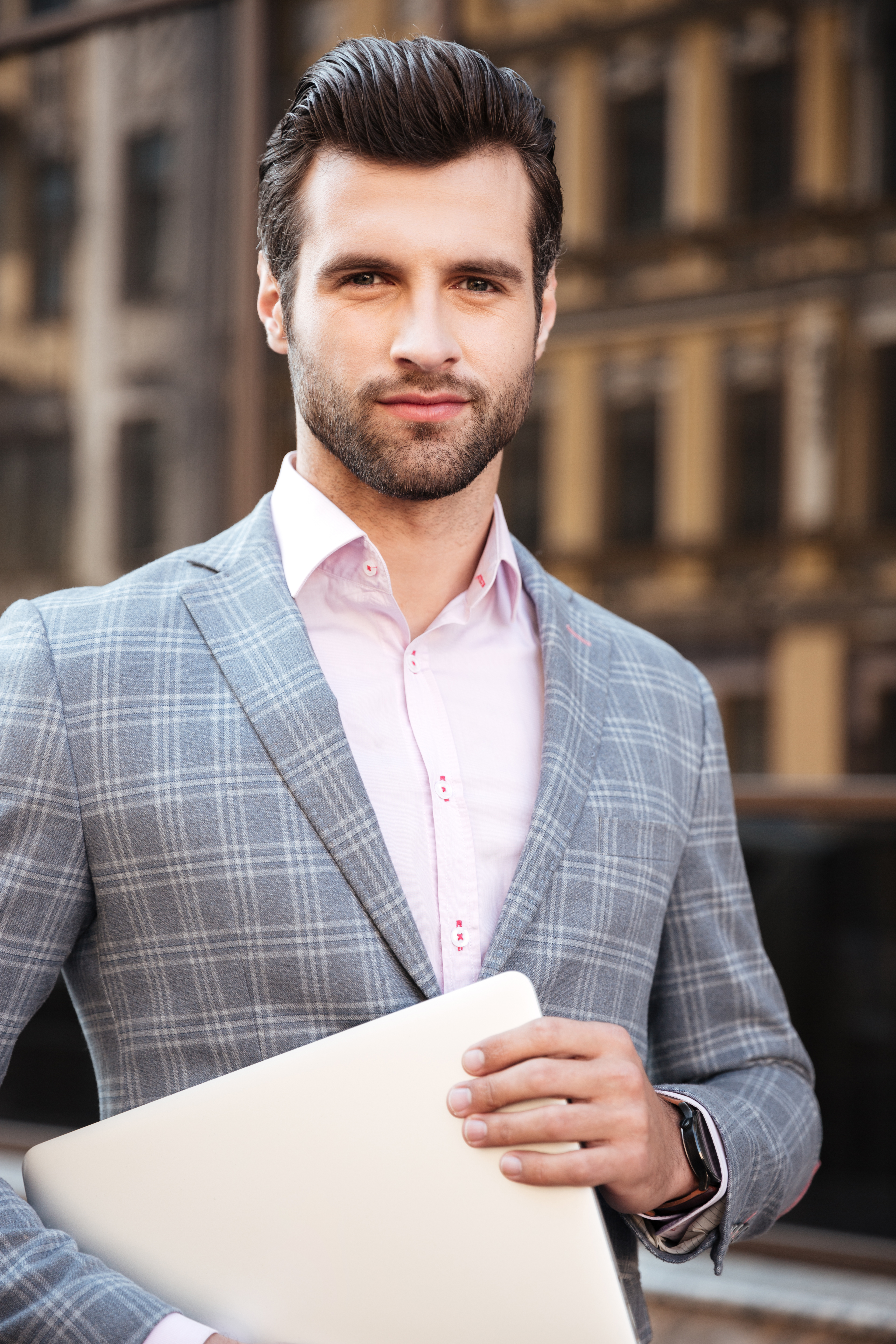 Portrait of a young handsome man in jacket holding laptop